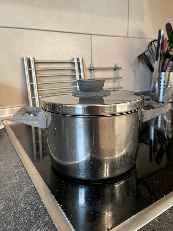 Energiesparen Ein großer Edelstahl-Schnellkochtopf mit Verriegelungssystem steht auf einem Herd in einer modernen Küche. Im Hintergrund sind Fliesen und weitere Küchengeräte zu sehen.