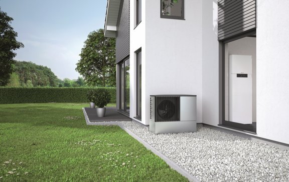 Wärmepumpe Moderne Luft-Wasser-Wärmepumpe der Marke Viessmann im Garten eines Einfamilienhauses, installiert auf einem Kiesbett direkt neben der Hauswand. Im Hintergrund sichtbar: großzügige Rasenfläche, Hecke und Bäume.
